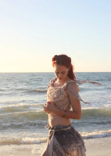 portrait of pretty female ship wrecked  model wearing  torn dress.  posing on the rocky  Ocean shoreline at sunset,