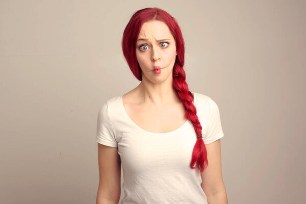 крупным планом портрет красивой женщины-модели с рыжими волосами в косе, выражающей эмоции над верхним выражением лица на студийном фоне.