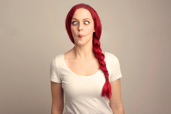 крупным планом портрет красивой женщины-модели с рыжими волосами в косе, выражающей эмоции над верхним выражением лица на студийном фоне.