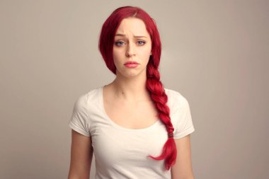 Örgülü kızıl saçlı güzel bir kadın modelin portresi stüdyo arkaplanındaki yüz ifadesi üzerinden duygularını ifade ediyor..