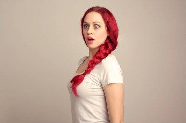 Örgülü kızıl saçlı güzel bir kadın modelin portresi stüdyo arkaplanındaki yüz ifadesi üzerinden duygularını ifade ediyor..