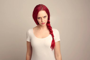 Örgülü kızıl saçlı güzel bir kadın modelin portresi stüdyo arkaplanındaki yüz ifadesi üzerinden duygularını ifade ediyor..