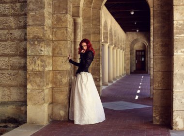 Kızıl saçlı güzel gotik bir elbise giyen, romantik kale taşı mimarisi geçmişi olan, uzun boylu bir kadın portresi..
