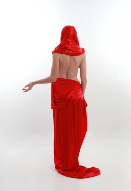 Kızıl saçlı, güzel, ipek bir elbise giyen, yaratıcı kol hareketleriyle ayakta duran beyaz stüdyo arka planında izole edilmiş, uzun boylu bir kadın portresi..