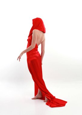 Kızıl saçlı, güzel, ipek bir elbise giyen, yaratıcı kol hareketleriyle ayakta duran beyaz stüdyo arka planında izole edilmiş, uzun boylu bir kadın portresi..