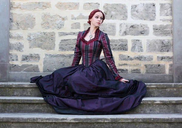 portrait of red-haired woman wearing a historical victorian gown costume, walking around beautiful location with stone architecture.