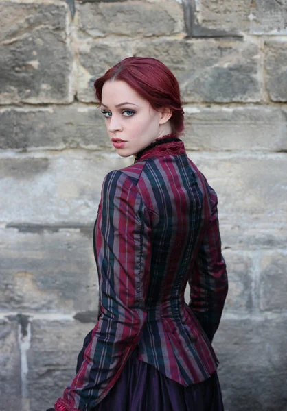 portrait of red-haired woman wearing a historical victorian gown costume, walking around beautiful location with stone architecture.