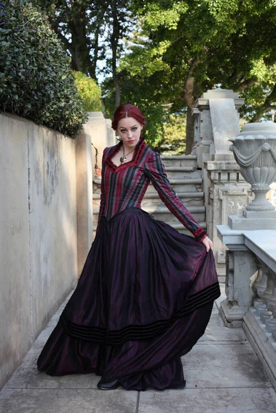 portrait of red-haired woman wearing a historical victorian gown costume, walking around beautiful location with stone architecture.