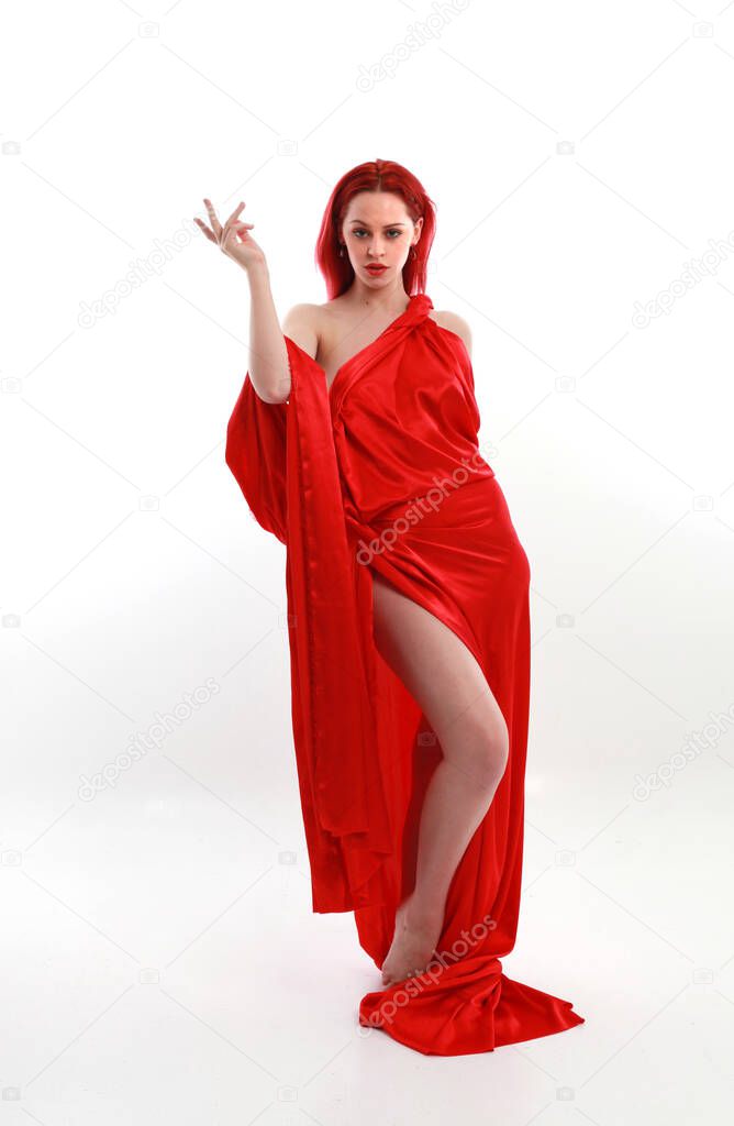 Full length portrait of red haired woman wearing a  beautiful sexy silk gown costume, standing pose with creative arm gestures, isolated on white studio background.