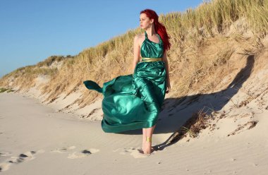 Yırtık gemi enkazı giymiş kızıl saçlı kadının tam boy portresi. Kayalık okyanus sahili arka planında el hareketleriyle poz vermek.