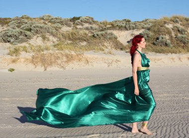 Full length portrait of  red haired woman wearing  torn shipwrecked clothing. Standing  pose with gestural hands at  rocky ocean beach landscape background. clipart