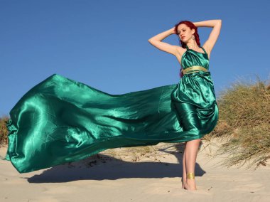 Yırtık gemi enkazı giymiş kızıl saçlı kadının tam boy portresi. Kayalık okyanus sahili arka planında el hareketleriyle poz vermek.