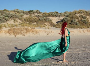 Yırtık gemi enkazı giymiş kızıl saçlı kadının tam boy portresi. Kayalık okyanus sahili arka planında el hareketleriyle poz vermek.