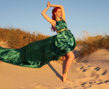 Yırtık gemi enkazı giymiş kızıl saçlı kadının tam boy portresi. Kayalık okyanus sahili arka planında el hareketleriyle poz vermek.