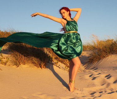 Yırtık gemi enkazı giymiş kızıl saçlı kadının tam boy portresi. Kayalık okyanus sahili arka planında el hareketleriyle poz vermek.