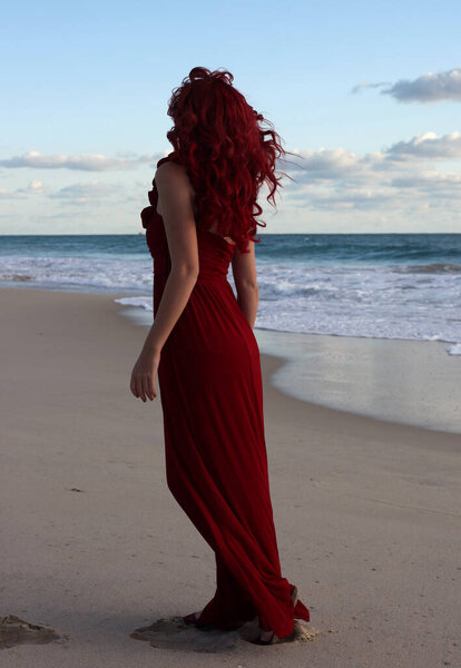 Полный портрет рыжеволосой женщины в элегантном красном платье. Стоя поза с жестом руки на закате океана пейзаж пляжа.