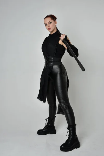 全长肖像漂亮的红头发女模特身穿黑色未来科幻皮衣 手持长矛武器 白色工作室背景上的动态站立姿势 — 图库照片