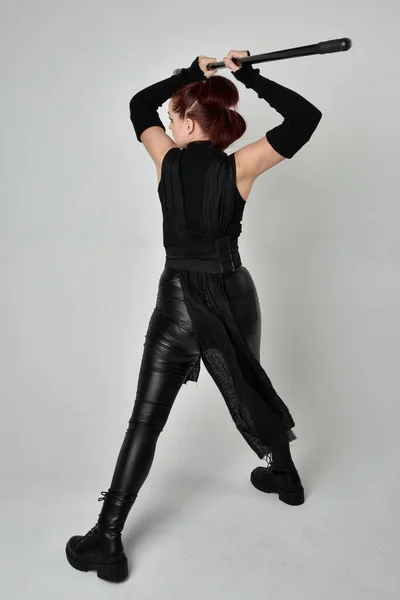全长肖像漂亮红头发的女模特身穿黑色未来科幻皮衣 手持长矛武器 动态站立姿势 面朝外 背向后 白色工作室背景 — 图库照片