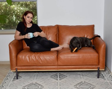 Tam boy portre o kızıl saçlı kız günlük giysiler giyen, rahat deri koltukta dinleniyor oturma odasında ev düzenleme.