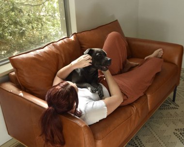 Tam boy portre o kızıl saçlı kız günlük giysiler giyen, rahat deri koltukta dinleniyor oturma odasında ev düzenleme.