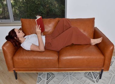 Tam boy portre o kızıl saçlı kız günlük giysiler giyen, rahat deri koltukta dinleniyor oturma odasında ev düzenleme.