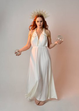portrait of beautiful red head woman wearing long flowing fantasy toga gown with golden halo crown jewellery,  posed on isolated on a white studio background. clipart