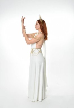 Kızıl saçlı güzel bir kadının portresi. Stüdyo arka planında meleksi altın haleler olan uzun, fantezi toga bir elbise giyiyor.