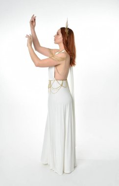 portrait of beautiful red head woman wearing long flowing fantasy toga gown with angelic  golden halo crown on studio background