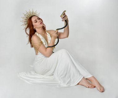 Kızıl saçlı güzel bir kadının portresi. Stüdyo arka planında meleksi altın haleler olan uzun, fantezi toga bir elbise giyiyor.