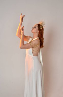 Kızıl saçlı güzel bir kadının portresi. Stüdyo arka planında meleksi altın haleler olan uzun, fantezi toga bir elbise giyiyor.