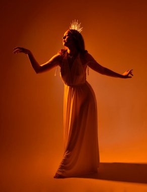 Kızıl saçlı güzel bir kadının portresi. Stüdyo arka planında meleksi altın haleler olan uzun, fantezi toga bir elbise giyiyor.