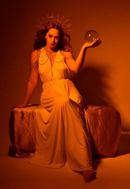 Kızıl saçlı güzel bir kadının portresi. Stüdyo arka planında meleksi altın haleler olan uzun, fantezi toga bir elbise giyiyor.