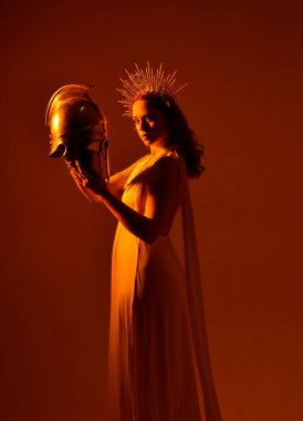 Kızıl saçlı güzel bir kadının portresi. Stüdyo arka planında meleksi altın haleler olan uzun, fantezi toga bir elbise giyiyor.