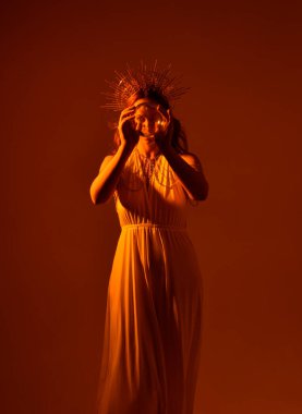 Kızıl saçlı güzel bir kadının portresi. Stüdyo arka planında meleksi altın haleler olan uzun, fantezi toga bir elbise giyiyor.