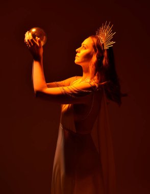 portrait of beautiful red head woman wearing long flowing fantasy toga gown with angelic  golden halo crown on studio background