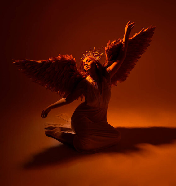 портрет красивой рыжеволосой женщины в длинном фэнтези тога платье с ангельской золотой венцом гало на студийном фоне