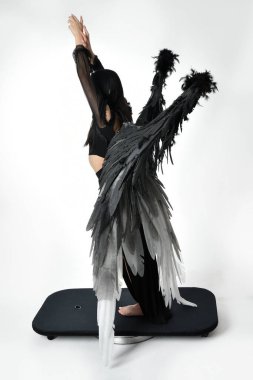 full length portrait of beautiful asian model with dark hair, wearing black gothic skirt costume, angel feather wings with horned headdress. Standing pose  isolated on studio background.