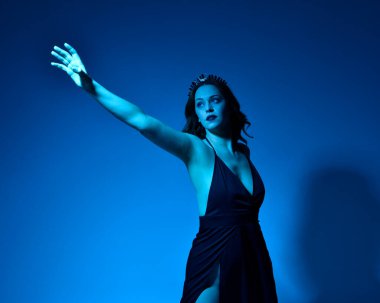 Zarif siyah elbise ve taç giyen güzel bir kadın modelin yakın plan portresi, fantezi dolu kol hareketleriyle bir stüdyo arka planına poz vermek, çok renkli yaratıcı ışıklandırma..