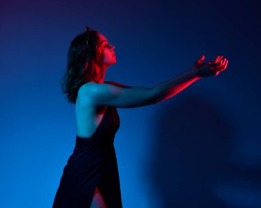 Zarif siyah elbise ve taç giyen güzel bir kadın modelin yakın plan portresi. Stüdyonun arka planında insan kafatası destekli fantezi jestlerle poz veriyor. çok renkli yaratıcı ışıklandırma.