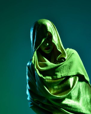 Zarif siyah elbise giyen, kapüşonlu bir pelerin giyen, fantezi dolu bir stüdyo arka planına poz veren güzel kadın modelinin yakın portresi..