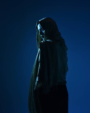 Zarif siyah elbise giyen, kapüşonlu bir pelerin giyen, fantezi dolu bir stüdyo arka planına poz veren güzel kadın modelinin yakın portresi..