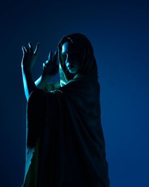 Zarif siyah elbise giyen, kapüşonlu bir pelerin giyen, fantezi dolu bir stüdyo arka planına poz veren güzel kadın modelinin yakın portresi..