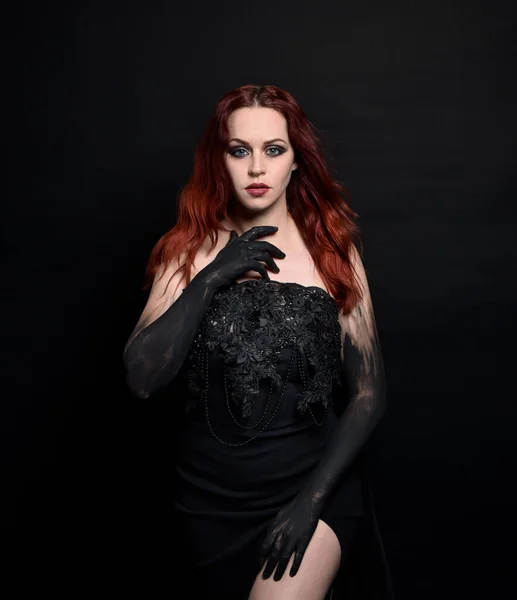 close up portrait of beautiful woman with red hair, wearing black dress with  elegant gestural hand poses on a dark studio background with moody lighting.