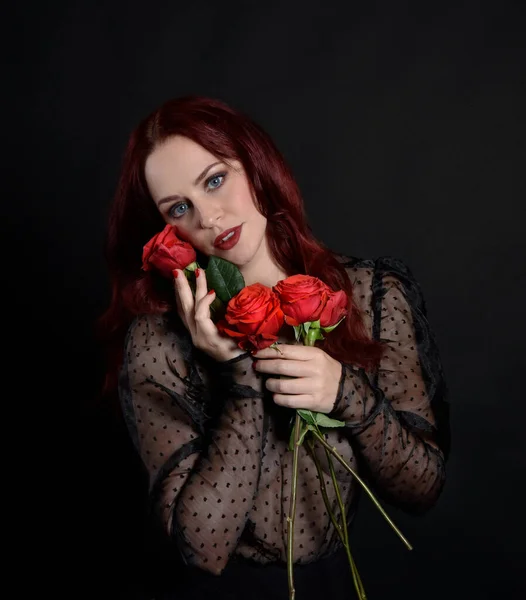 close up portrait of beautiful woman with red hair, wearing black dress with  elegant gestural hand poses on a dark studio background with moody lighting.