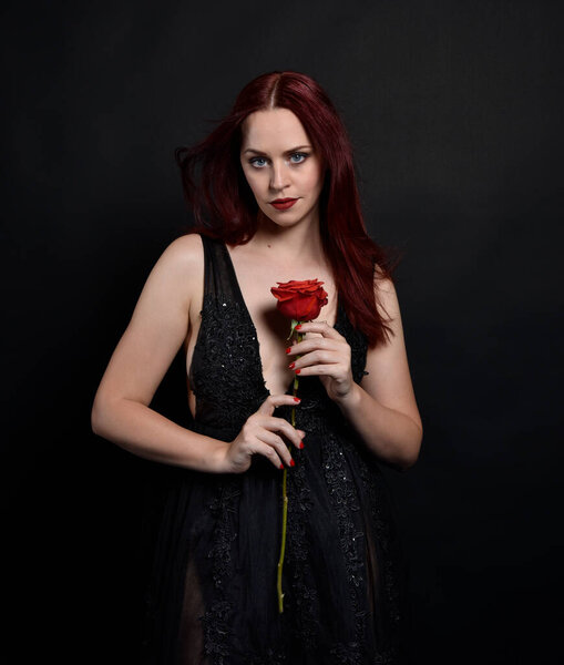 крупным планом портрет красивой женщины с рыжими волосами, в черном платье с элегантными жестикулярными позами рук на темном фоне студии с капризным освещением.