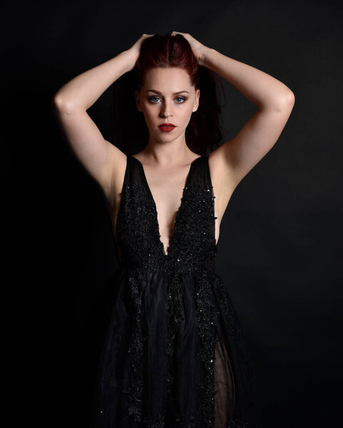 close up portrait of beautiful woman with red hair, wearing black dress with  elegant gestural hand poses on a dark studio background with moody lighting.