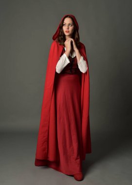 Full length portrait of beautiful brunette woman wearing red medieval fantasy costume with long skirt and flowing hooded cloak.Standing pose with gestural hand poses, isolated on grey studio background. clipart