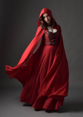Full length portrait of beautiful brunette woman wearing red medieval fantasy costume with long skirt and flowing hooded cloak.Standing pose with gestural hand poses, isolated on grey studio background. clipart