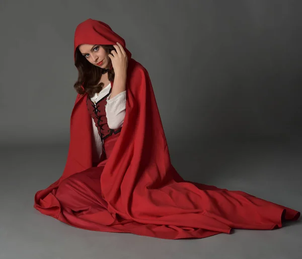 穿着红色中世纪奇幻服装 长裙和飘逸的帽衫的漂亮黑发女人的全长肖像 以手势式手姿坐姿 与灰色画室背景隔离 — 图库照片