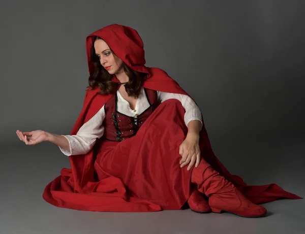 穿着红色中世纪奇幻服装 长裙和飘逸的帽衫的漂亮黑发女人的全长肖像 以手势式手姿坐姿 与灰色画室背景隔离 — 图库照片